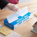 A person in plastic gloves using Durable Packaging deli wrap to cut cheese on a table.