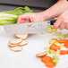 A person using a Mercer Culinary Nakiri knife to cut carrots on a cutting board.