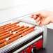 A hand holding hot dogs in an Avantco hot dog roller grill.