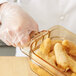 A person wearing plastic gloves holding a Carlisle amber plastic food pan of fried food.