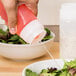 A hand pouring liquid from a Tablecraft Invertatop squeeze bottle onto a bowl of salad.