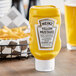 A Heinz upside down yellow mustard squeeze bottle next to a basket of fries.