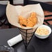A wire cone basket lined with a Choice natural kraft paper bag holding fried chicken.