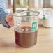 A hand using a WebstaurantStore clear plastic measuring cup to pour brown liquid.