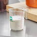 A WebstaurantStore clear plastic measuring cup filled with milk on a counter.