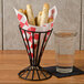 A black metal cone basket with a red and white checkered paper inside holding food with a glass of water.