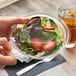 A hand holding a salad in a Polar Pak clear plastic bowl with a lid.