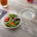 A Polar Pak clear plastic bowl filled with salad with a fork and knife on the side.