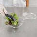 A gloved hand uses a spoon to add lettuce to a Polar Pak clear plastic bowl with a lid.