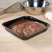 A brownie in a Solut black square paperboard pan on a counter.