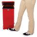 The lower half of a person's body standing next to a red Rubbermaid medical waste step can.