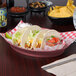 An oval raspberry polypropylene deli server filled with a group of tacos on a table.