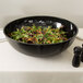 A black Cambro Camwear round ribbed bowl filled with salad on a table.