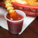 A french fry being dipped in Solo translucent plastic portion cup of ketchup.