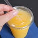 A hand placing a clear plastic lid with a straw slot on a Solo plastic cup filled with yellow liquid.