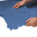 A man's hands holding a blue plastic Cactus Mat interlocking floor tile.