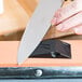 A person's hand sharpening a knife with a Victorinox Norton Multi-Oilstone.