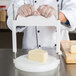 A person using white gloves to cut cheese with a Matfer Bourgeat cheese slicer on a white plate.