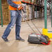 A man in an orange vest using a Hoover L1405 Brush SpinSweep Pro floor sweeper in a warehouse.