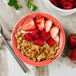 A red Tuxton Cinnebar monkey dish filled with strawberries, granola, and yogurt.