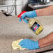A person wearing blue gloves uses Windex multi-surface cleaner to clean a professional kitchen counter.