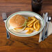 A Homer Laughlin green banded oval platter with a plate of food, a burger, lettuce, and tomato on a table.