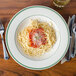 A close up of a Homer Laughlin green banded pasta bowl filled with spaghetti and sauce with parmesan cheese on a table.