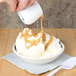 A person pouring caramel sauce into a Homer Laughlin green banded fruit bowl of ice cream.