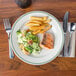 A Homer Laughlin Green Band plate with salmon, fries, and salad with a fork next to it.