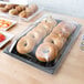 A 12" x 20" black polycarbonate tray filled with bagels and pastries on a table.