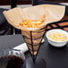 Choice natural kraft paper bag in a black metal cone basket filled with french fries.