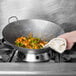 A hand holding a white dish towel over a Town hand hammered Cantonese wok filled with shrimp and vegetables cooking on a stove.