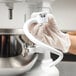 A person in gloves using a KitchenAid mixer with a white coated dough hook.