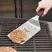A Mercer Culinary Hell's Handle spatula with a square edge flipping a hamburger patty.