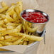 A bucket of french fries with a bowl of ketchup on a white background.