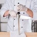 A chef in a white uniform using a Mercer Culinary knife sharpening steel to sharpen a knife.