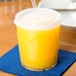 A close up of a Dinex clear plastic tumbler filled with orange juice and a straw.