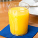 A close up of a Dinex clear plastic tumbler filled with orange juice on a table.