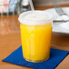 A clear plastic Dinex tumbler with a straw and orange liquid on a blue napkin.