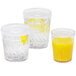 Three Dinex clear plastic tumblers with orange juice and lemon slices on a white background.
