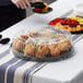 A person serving food in a Visions plastic round catering tray with a high dome lid on a table.