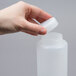 A hand holding a white plastic squeeze bottle with a thin dispensing valve.