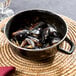 A black enameled steel pot with a lid filled with mussels on a table.