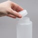 A hand holding a white plastic squeeze bottle with a thick valve lid.