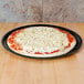 A Solut black oven safe pizza tray with a pizza with cheese on it.