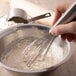 A hand whisking white rice flour in a bowl.