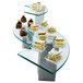An Eastern Tabletop quarter circle tempered glass buffet shelf on a table with different desserts on it.