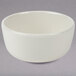 A Tuxton eggshell china bowl with a small rim on a gray surface.