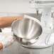 A person in gloves holding a stainless steel KitchenAid mixing bowl.
