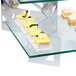 A glass table with a group of cakes on a glass shelf with Eastern Tabletop stainless steel "L" shaped corners.